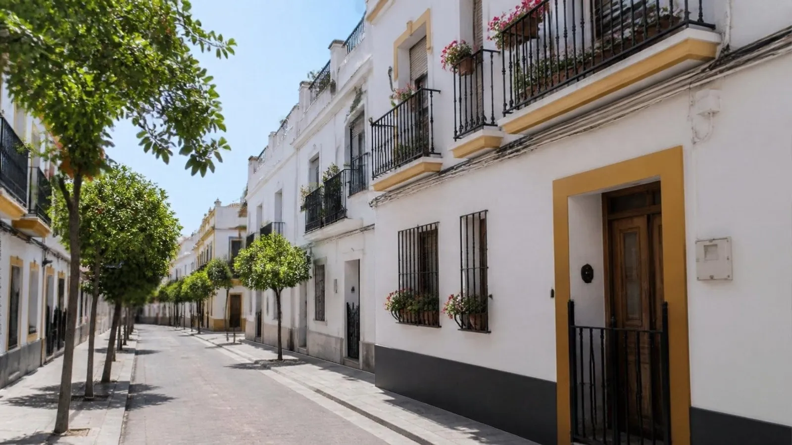 Calle de casas blancas con balcones de forja y naranjos en un barrio residencial de Córdoba
