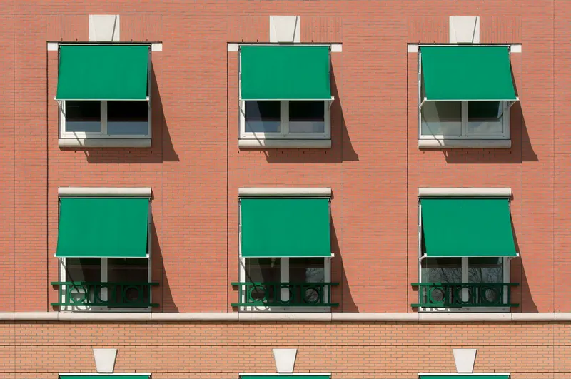 Toldos de punto recto verdes en las ventanas de un edificio de viviendas
